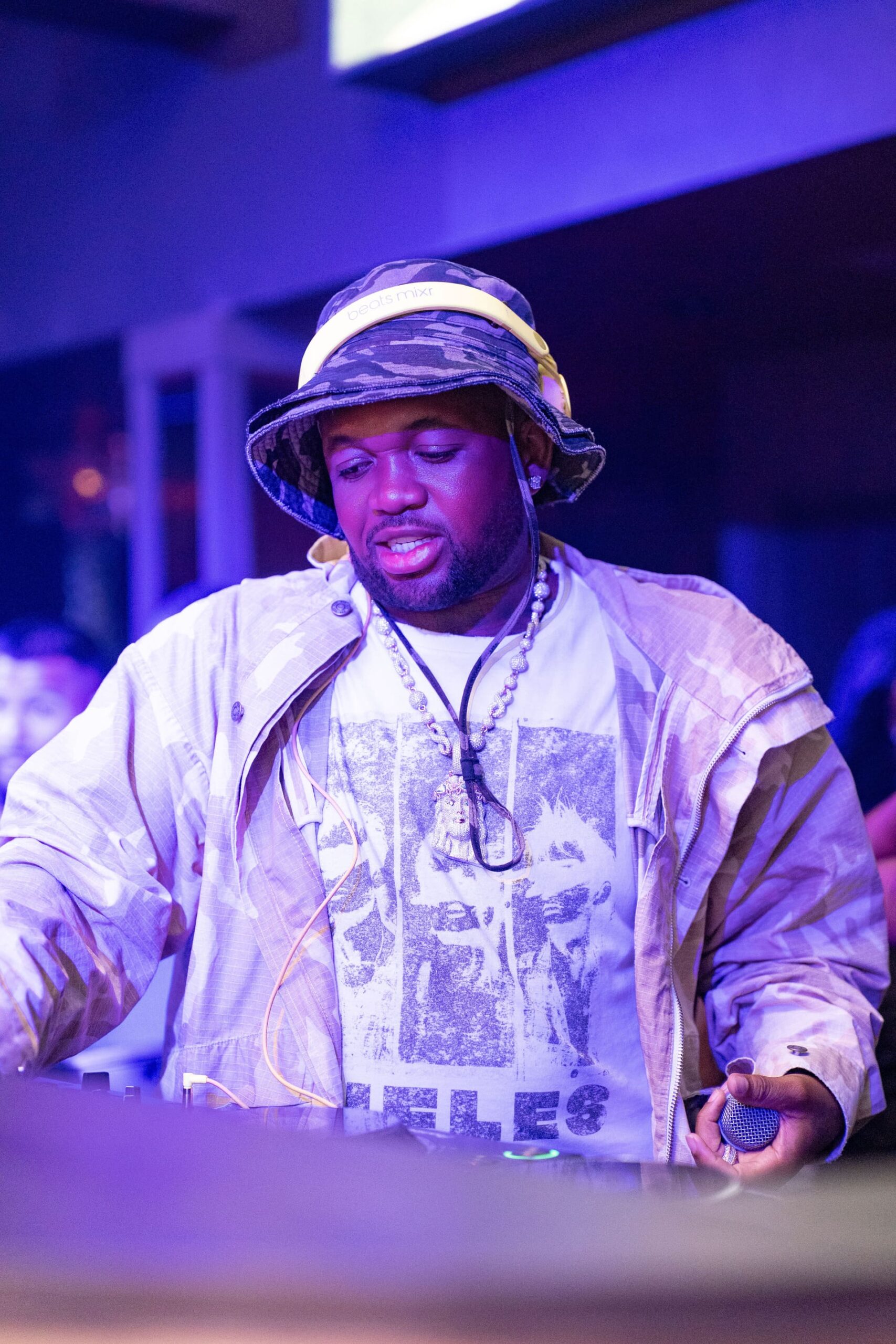 Man wearing a camo bucket hat and yellow headphones while performing as a DJ at a nightclub.
