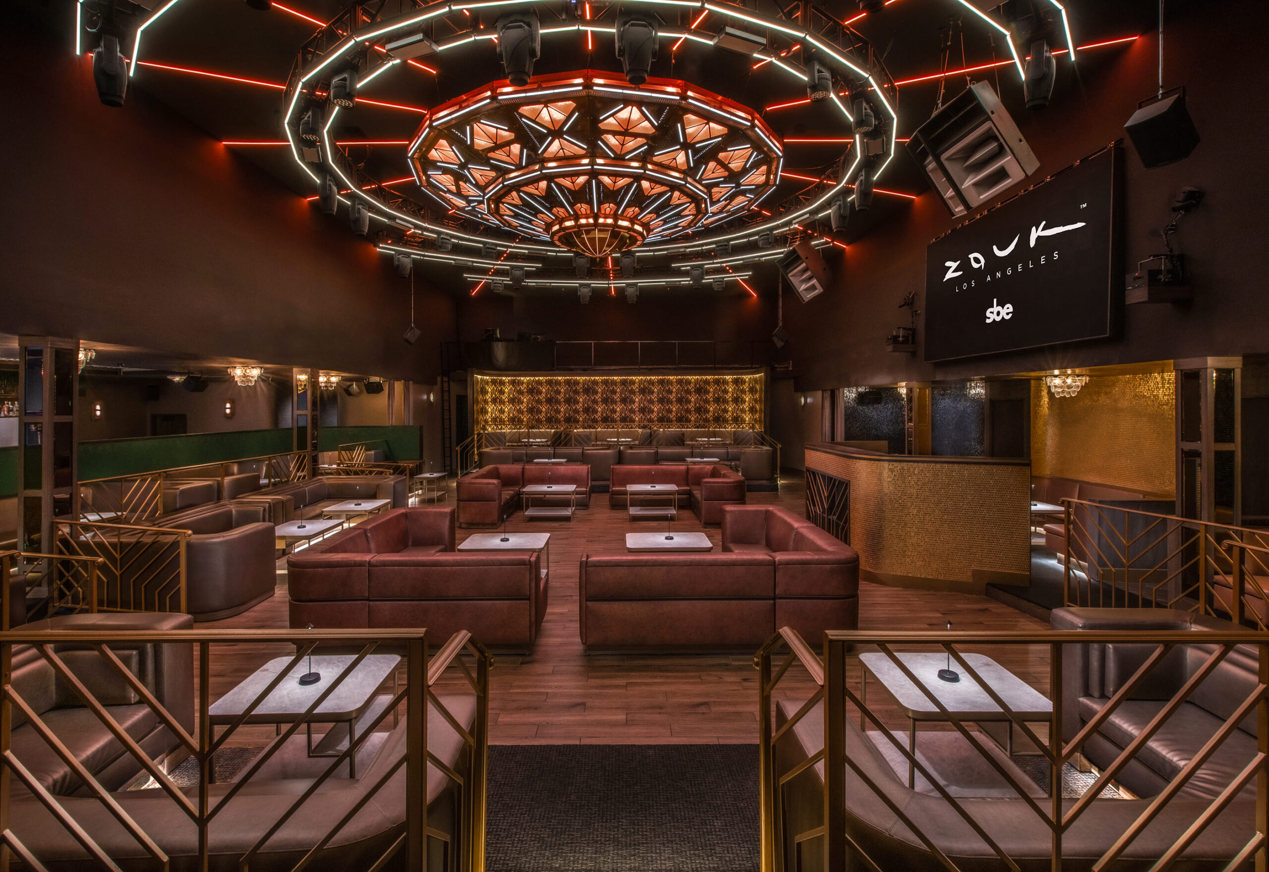 Empty nightclub lounge with leather booths, a patterned ceiling fixture, and ambient lighting.