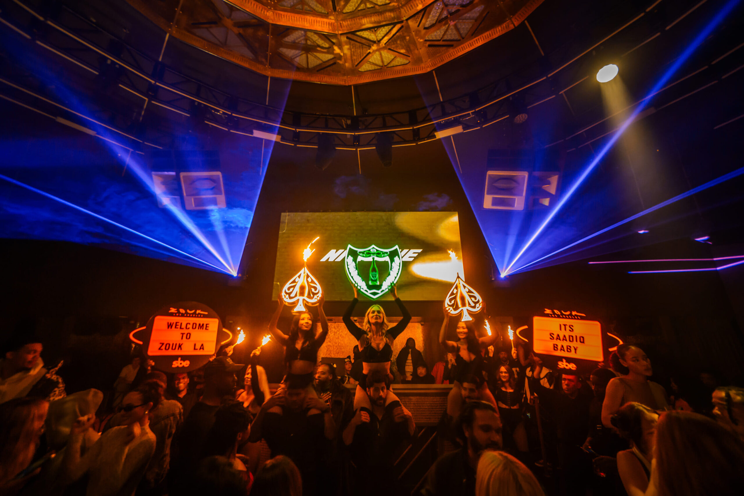 Performers with LED signs and sparklers entertain a packed crowd under laser lights and a domed ceiling at Zouk LA.