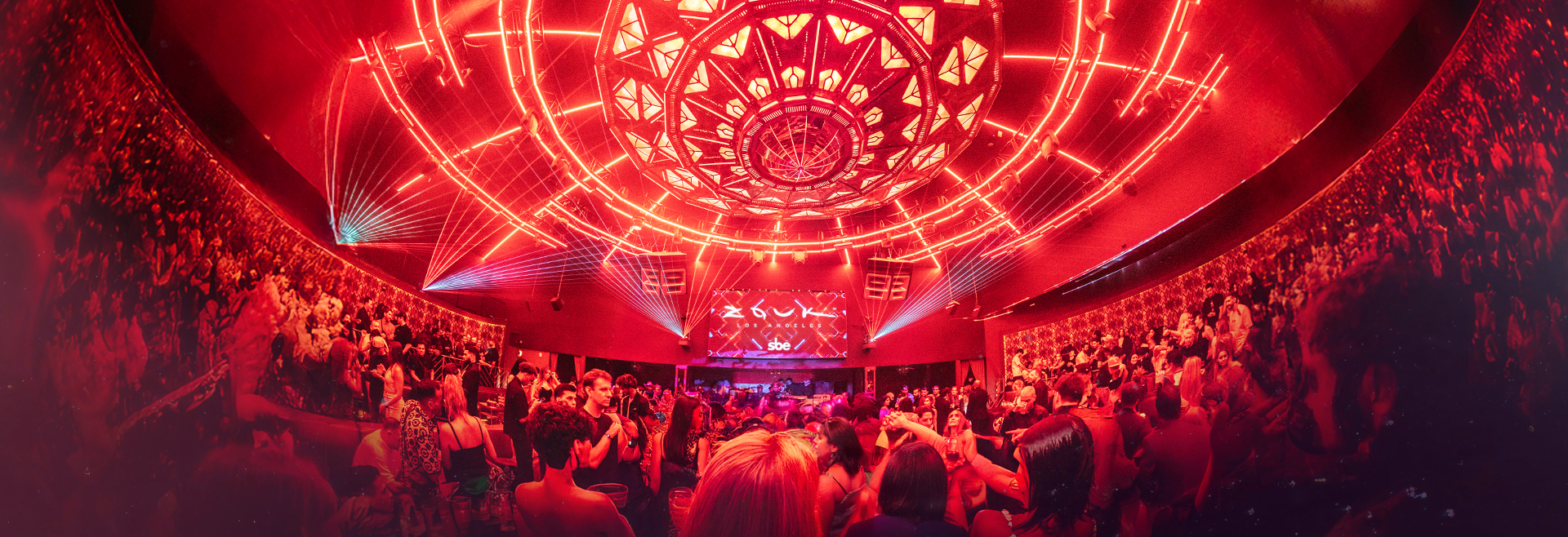 Vibrant crowd inside Zouk Los Angeles under a red-lit ceiling with geometric LED designs and laser beams.